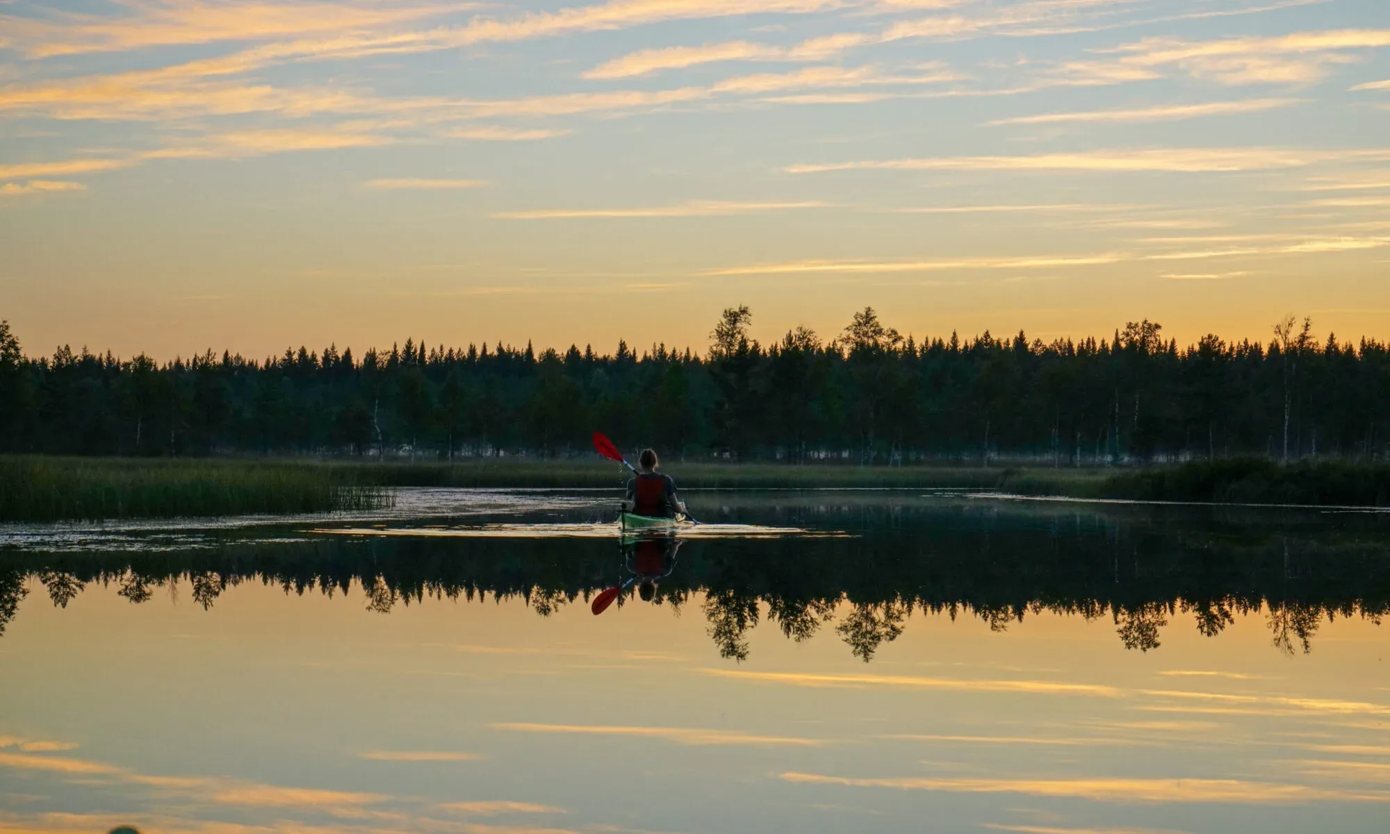 Kajak i solnedgången på en spegelblank sjö. Eldgul himmel.